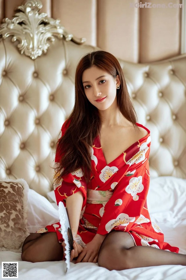 A woman in a red kimono sitting on a bed.