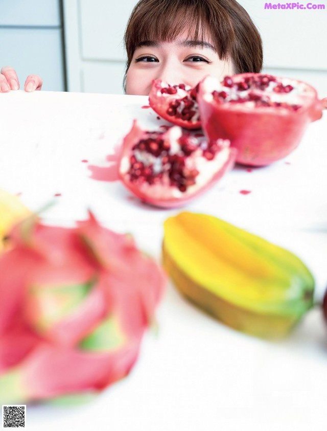 A woman peeking over a table with a pomegranate and a mango.