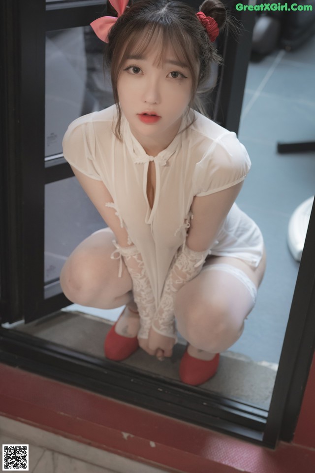 A woman in a white shirt and red shoes crouching on a window sill.