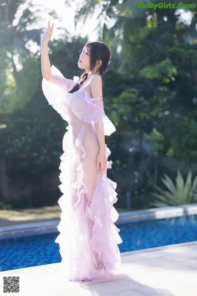 A woman in a pink dress standing next to a swimming pool.