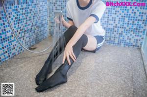 A woman sitting on the floor in a bathroom next to a shower.