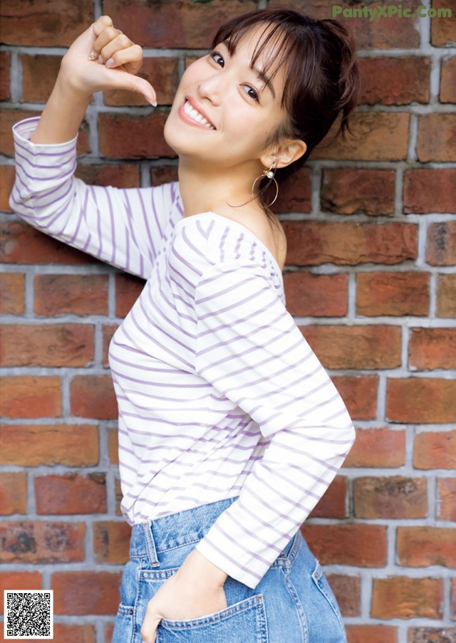 A woman leaning against a brick wall with her hand on her hip.