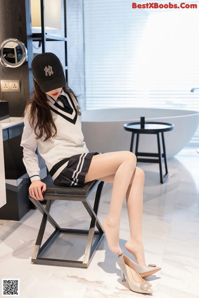 A woman sitting on a stool wearing a baseball cap.