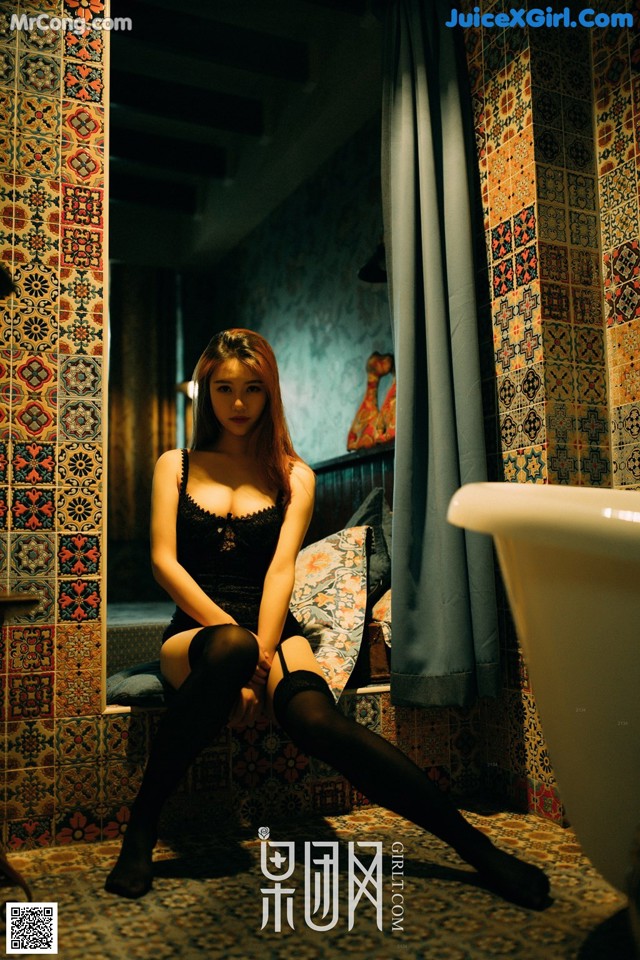 A woman sitting on a bed in a bathroom next to a bathtub.