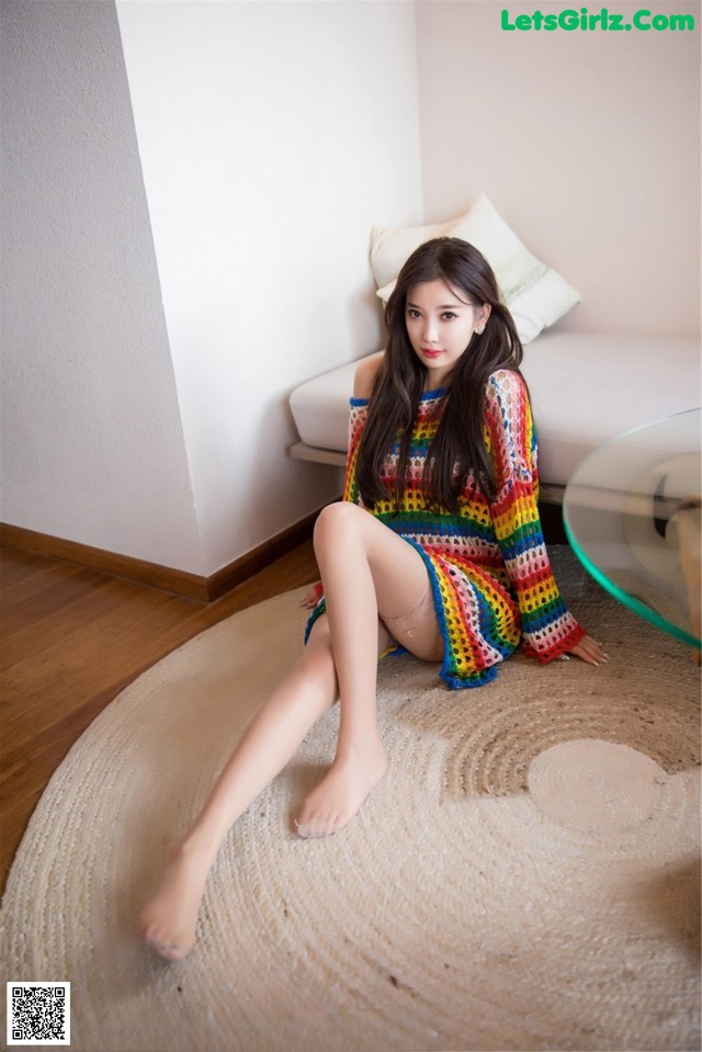 A woman sitting on the floor in a colorful dress.