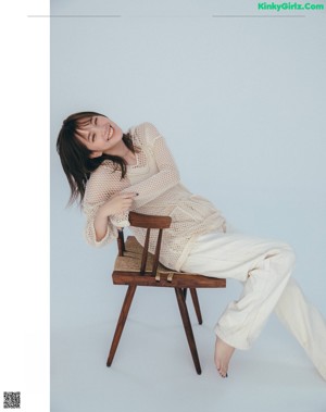 A woman sitting on a wooden chair with her hand on her chin.