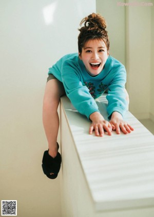 A woman in a blue sweater leaning on a white table.