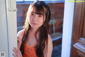 A young woman in an orange top and white panties posing for a picture.