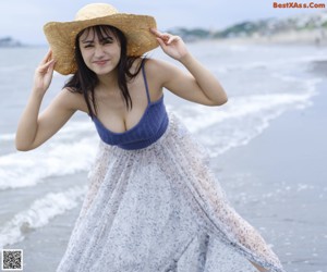 A woman walking on the beach with a hat on.