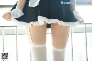 A woman in a maid outfit sitting on a bed.