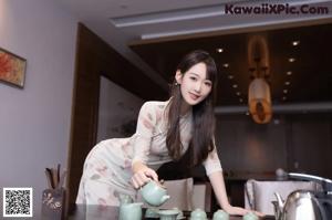 A woman in a kitchen preparing tea on a stove.