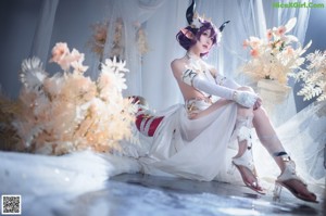 A woman in a white dress sitting on a bed.