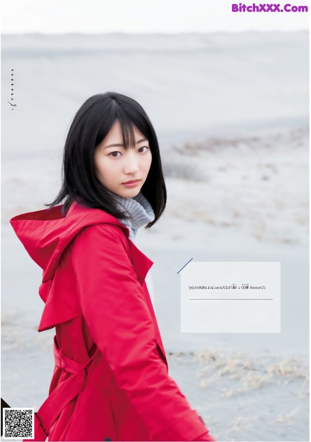 A woman in a red coat standing on a beach.