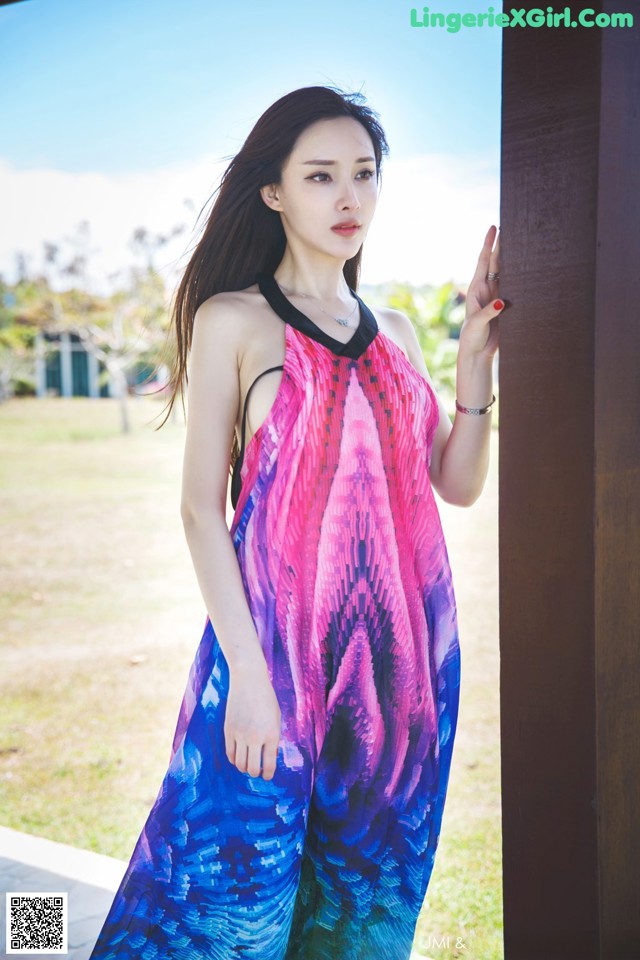 A woman in a colorful dress leaning against a wall.