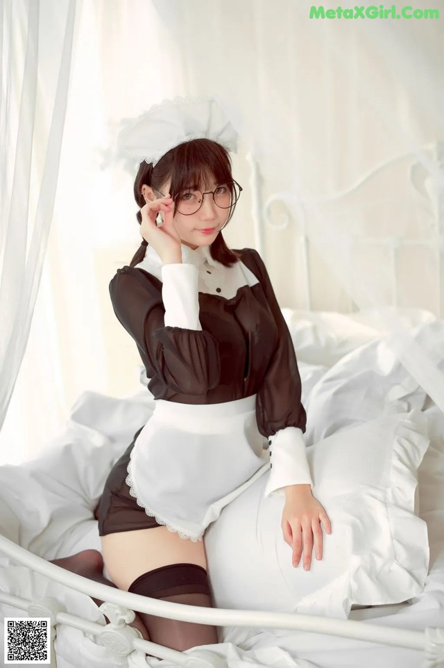 A woman in a maid outfit sitting on a bed.