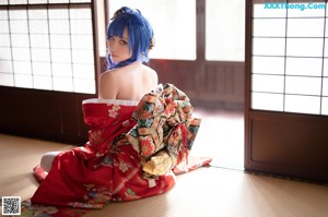 A woman in a red kimono sitting on a wooden floor.