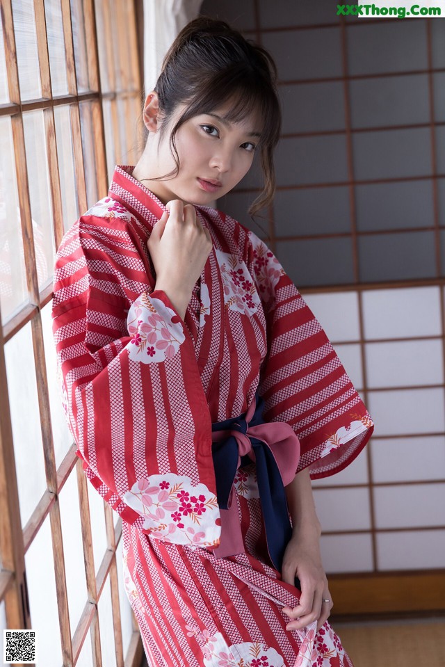 A woman in a red and white kimono leaning against a window.