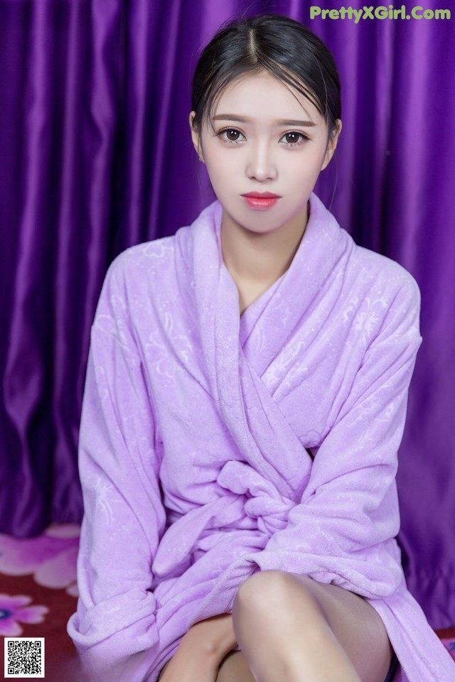 A woman in a purple robe sitting on a bed.