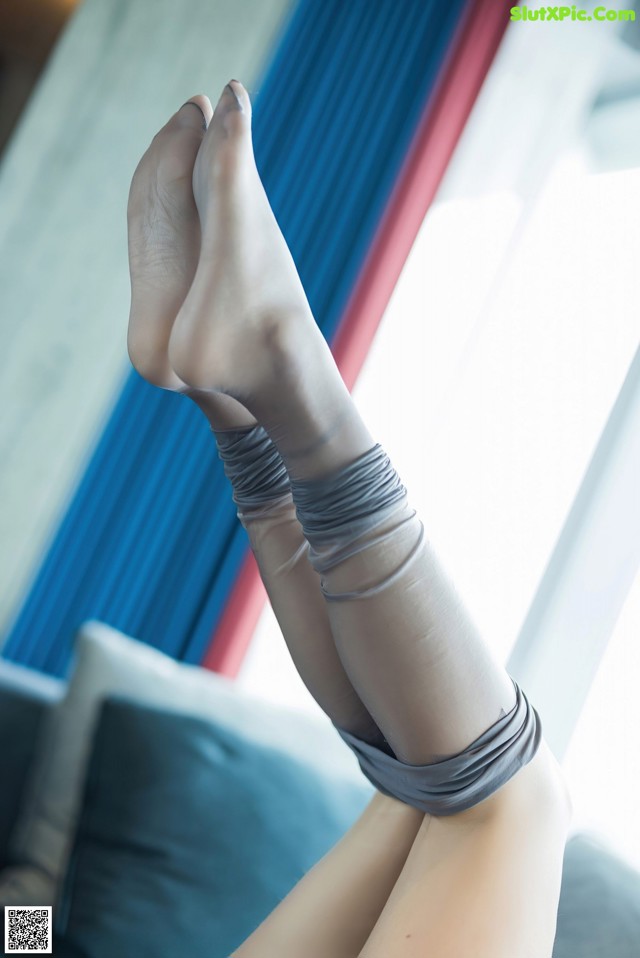 A woman's legs in gray stockings sitting on a couch.