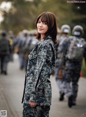 A woman in a military uniform salutes as she stands in front of an airplane.