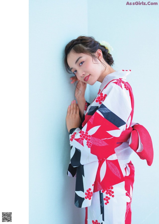 A woman in a red and white kimono leaning against a wall.