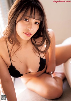 A woman in a black bra and panties sitting on a bed.