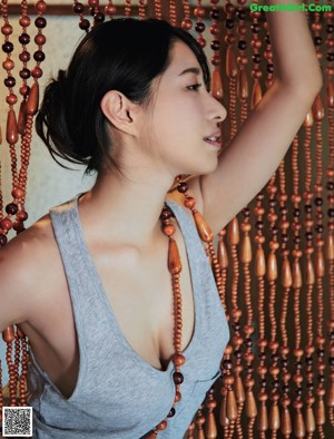 A woman in a gray tank top and pink panties standing in a shower.