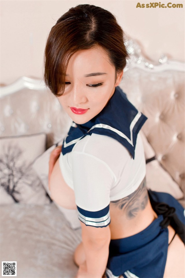 A woman in a sailor outfit is posing on a bed.