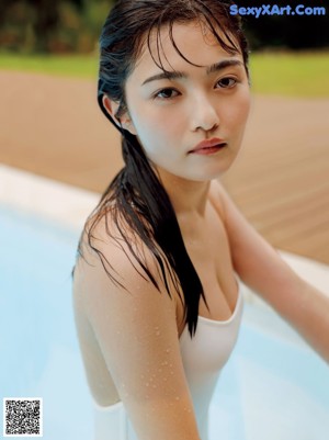 A woman in a white bodysuit sitting on a bed next to a pool.