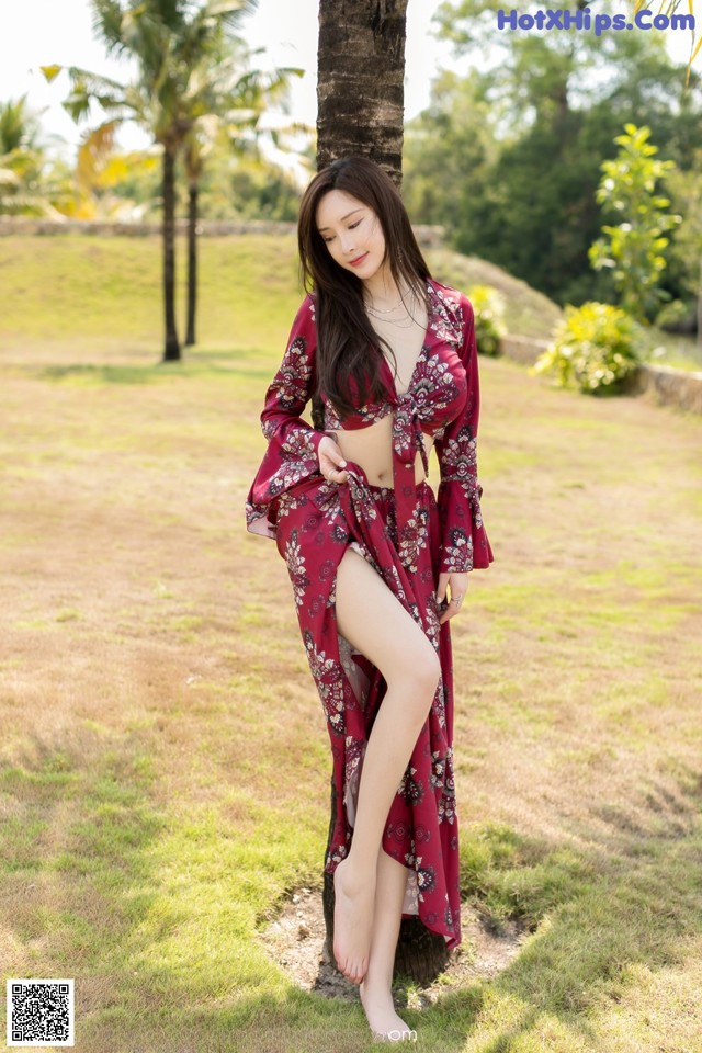 A woman in a red dress standing next to a palm tree.