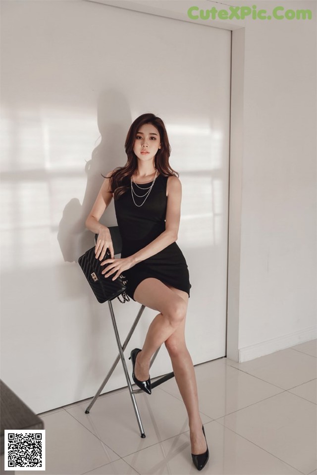 A woman in a black dress sitting on a chair.