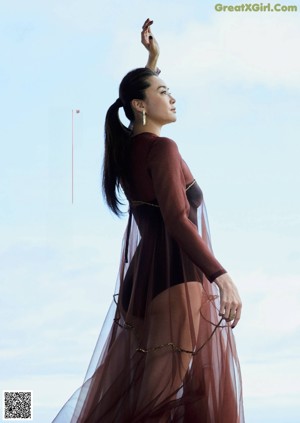 A woman in a black dress leaning against a wall.