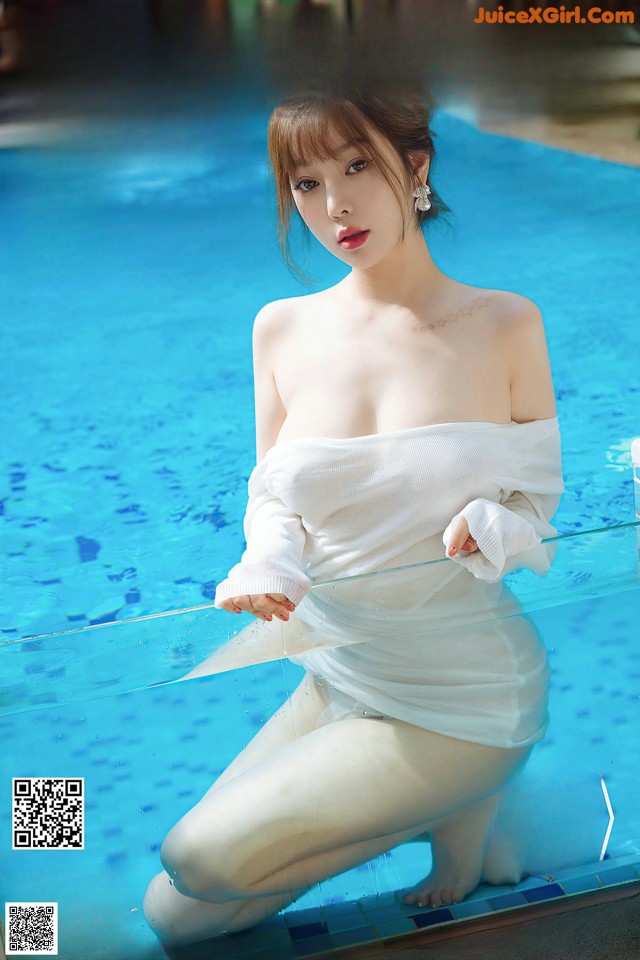 a woman in a white dress sitting on the edge of a pool