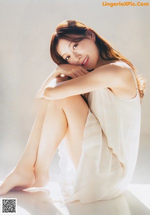 A woman in a white dress standing by a window.