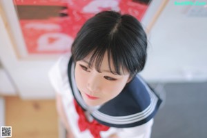 A woman in a school uniform sitting on a bed holding a drink.