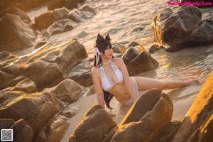 A woman in a white bikini sitting on a beach.