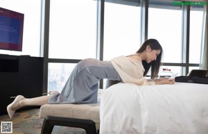 A woman in a white shirt is standing on a bed.