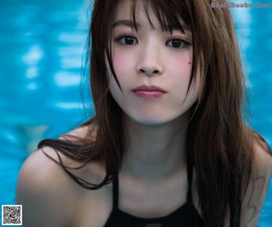 A woman in a black bikini posing by a pool.