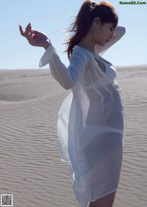 A woman in a black bathing suit standing next to a white horse.