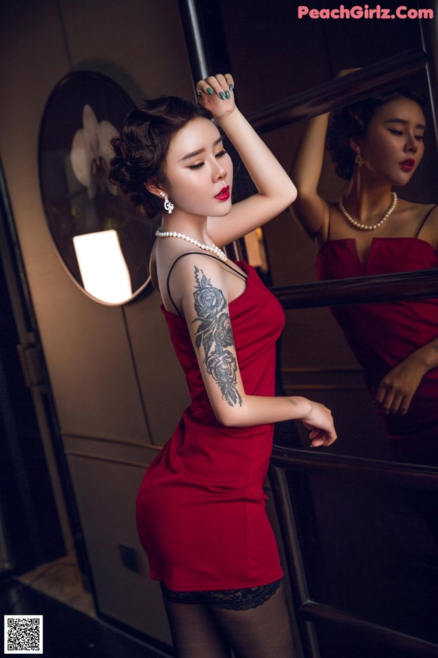 A woman in a red dress standing in front of a mirror.