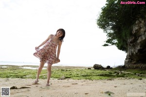 A woman in a floral dress standing on a beach.