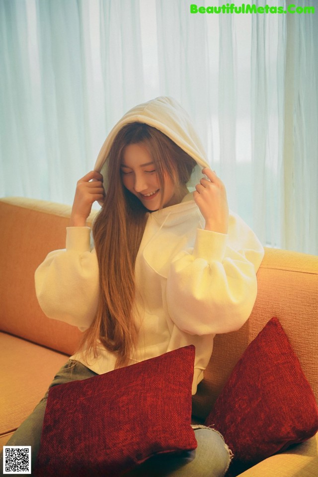 A woman sitting on a couch wearing a white hoodie.